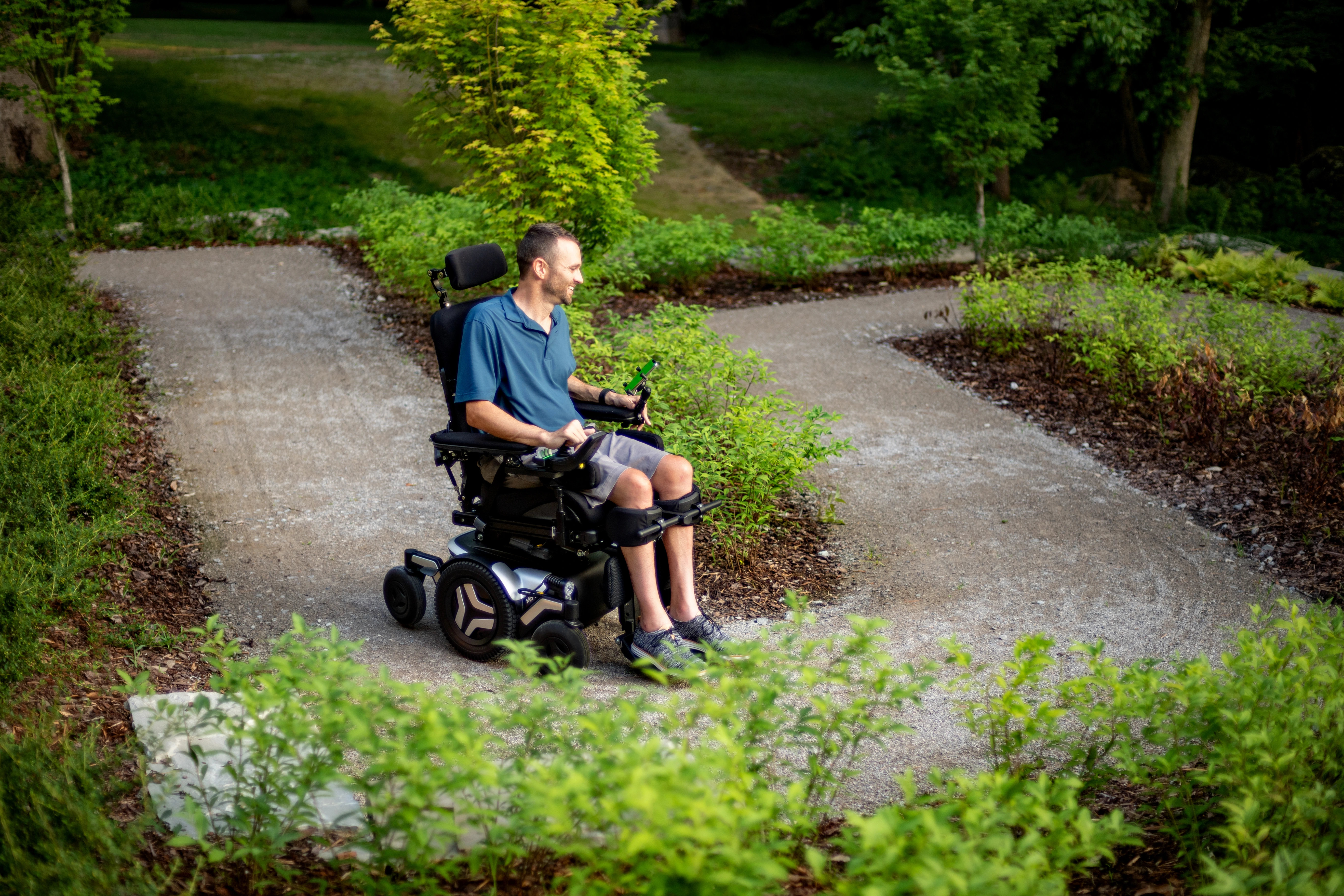 Man driving silver Permobil M5 wheelchair on winding path